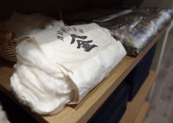 寝具専門店もりたけの店内に展示された、上質な国産真綿（シルク）素材の画像。海外産とは一線を画す養蚕からのこだわりを持ち、熟練の職人が繊細な繭を丹念に「手挽き」してふんわりと引き伸ばしています。この特別な真綿を使用し、生地も中身もシルク100％で仕立てた西川のオリジナル商品は、お肌に優しくしっとりと馴染む極上の肌触りを実現します。