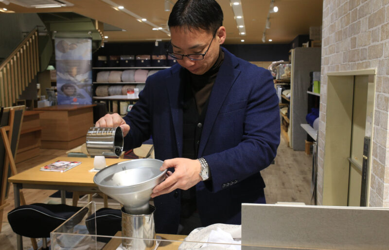 寝具と枕の専門店もりたけの店内風景。専門資格を持つスタッフ(ピローアドバイザー)が、計量カップと漏斗(ろうと)を使用し、オーダーメイド枕の中材を丁寧に入れて高さや寝心地を調整・作成している様子。