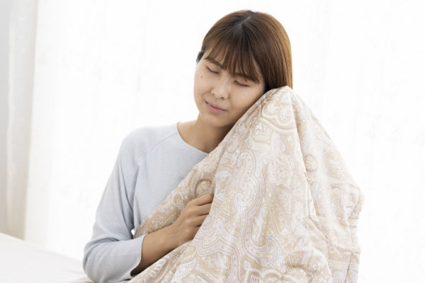 女性が柔らかなふとんを頬に当てて、心地よさそうにしている画像。寝具専門店もりたけがおすすめする「西川の国産真綿」ふとんは、熟練の職人による伝統の「手挽き」で仕上げられ、生地も中身もシルク100％を贅沢に使用しています。お肌に優しい「健康ふとん」として、お身体へしっとりと吸い付くように「しっくりと馴染む」極上の肌触りが特長です。羽毛ふとんの下に重ねるインナーケットとしても最高の温もりを発揮します。
